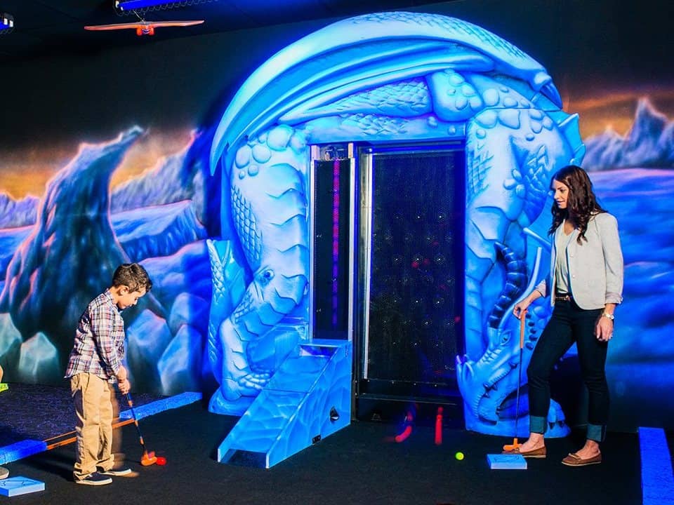 Mom and her son are playing mini putt in Dragon's Tale Blacklight Mini-Golf